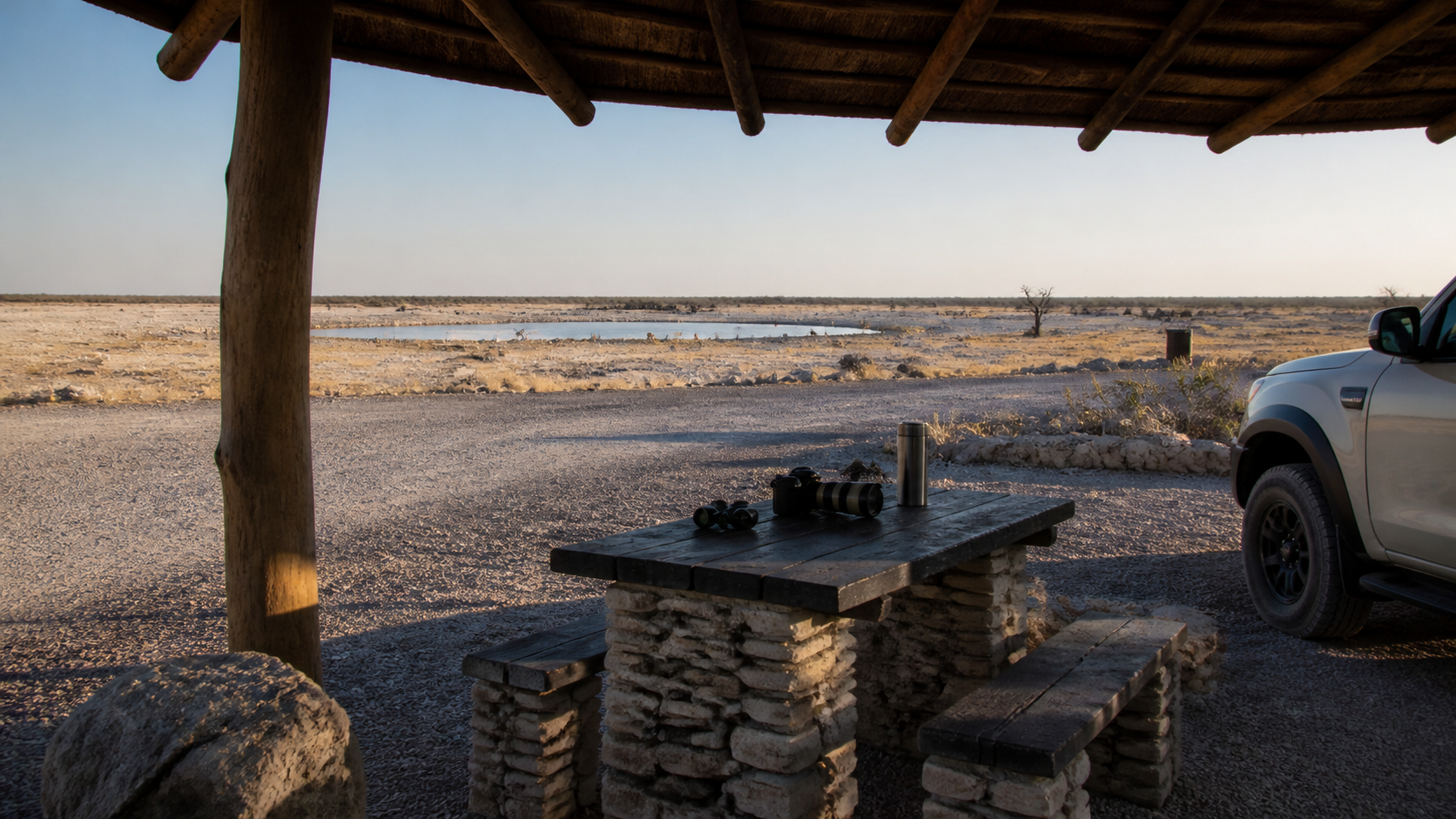 Etosha-Salzpfanne, Wasserstelle, Schotterweg und weiter namibischer Himmel mit Fokus auf Orientierung und ruhige Planung.