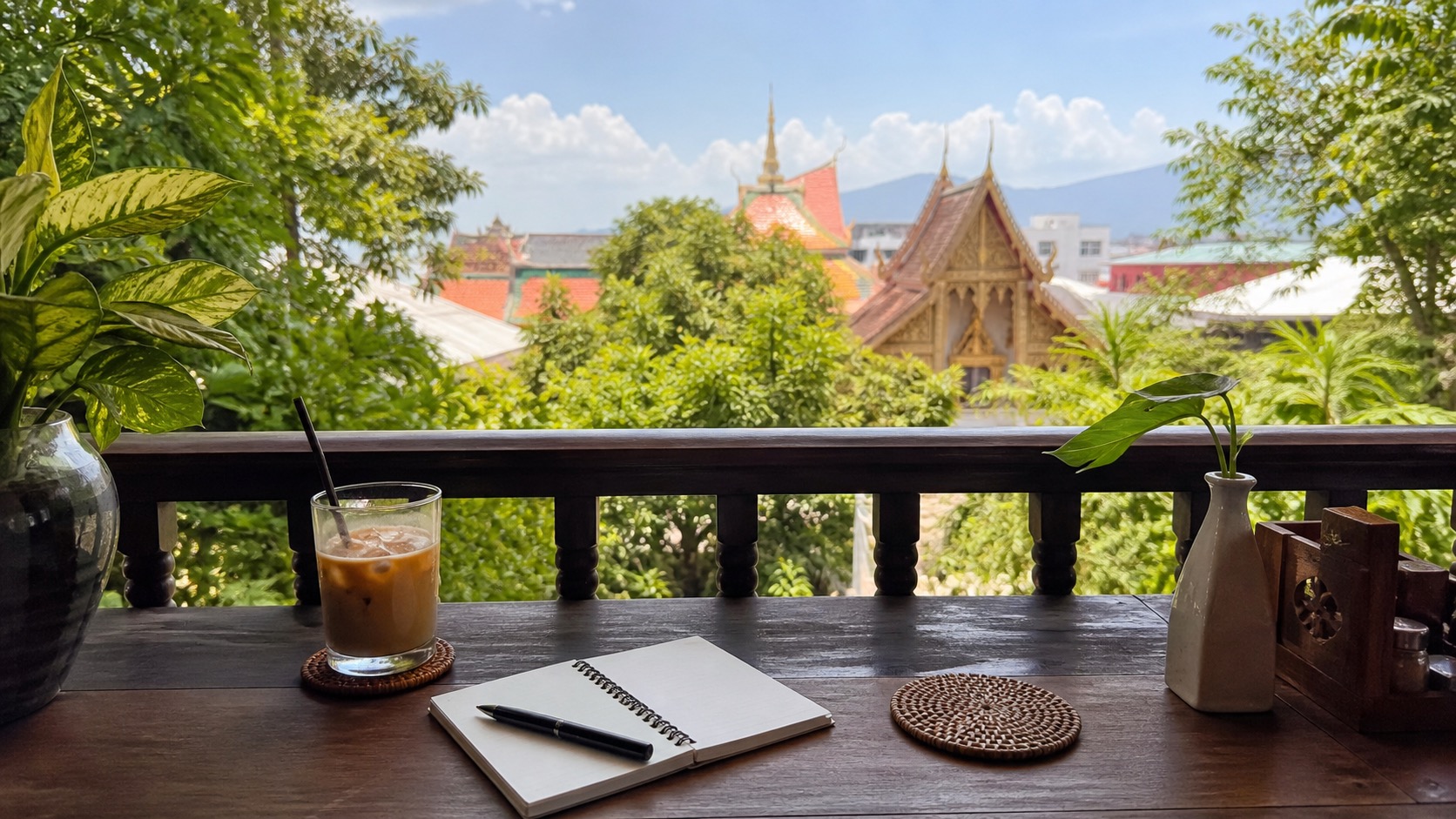 Caféterrasse in Chiang Mai mit leerem Notizbuch und Blick auf Tempeldächer