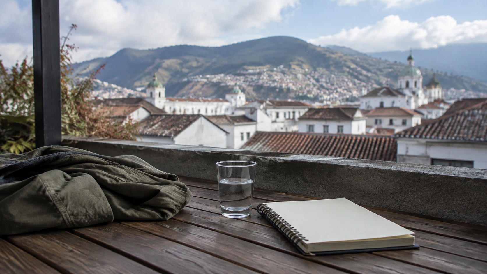Dachterrasse in Quito mit Wasser, Jacke und leerem Notizbuch vor Andenblick